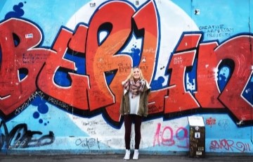 image of a student standing in front of a wall with the graffiti showing the words Berlin