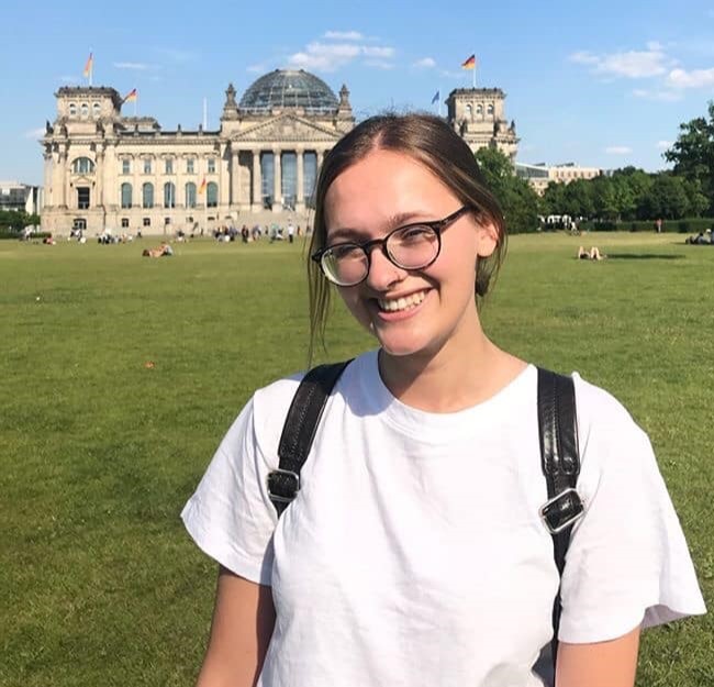 image of young woman standing in a sunny field with a large historic building in the background