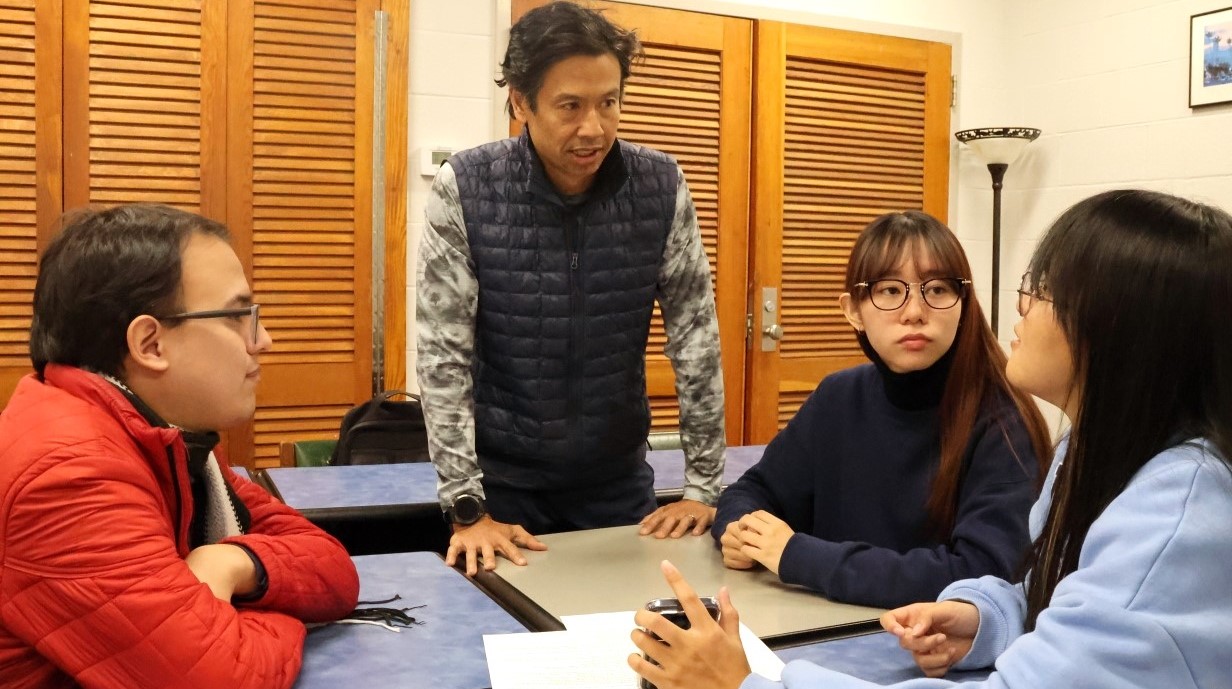 three students seated around a table with a professor talking with them