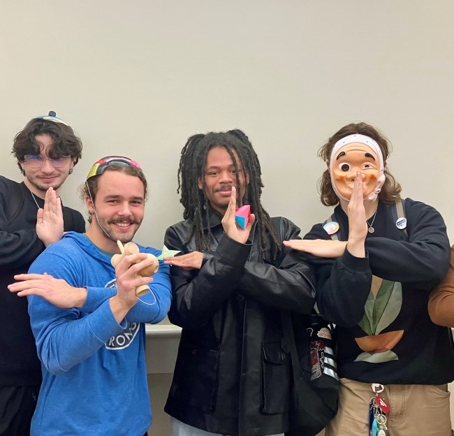 a few students with Japanese masks holding Japanese game pieces and making hand gestures to represent characters in a game