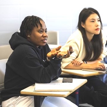 image of two students in a classroom, one talking and gesturing with her hands