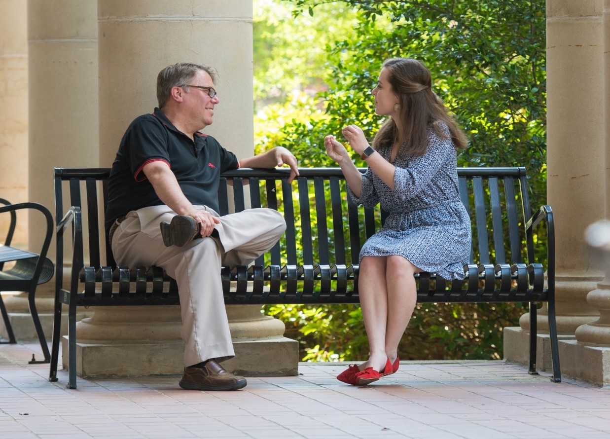 professor and a student sitting and talking on the front porch of a building