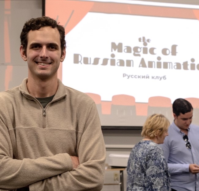 student smiling at the camera and in the background is a screen with the words for a Russian animation event