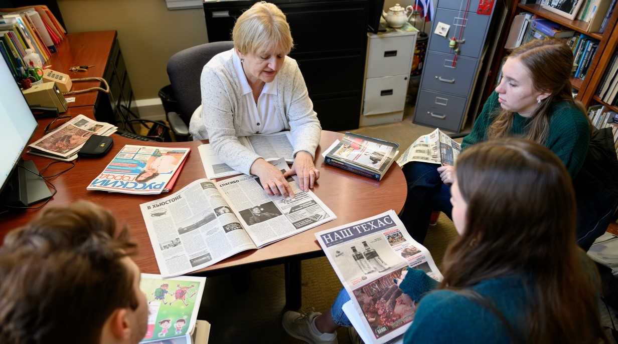 image of three students and professor seated together in professor's office and looking at foreign newspapers 