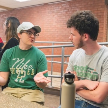 image of students seated at a table in a kitchen area talking.