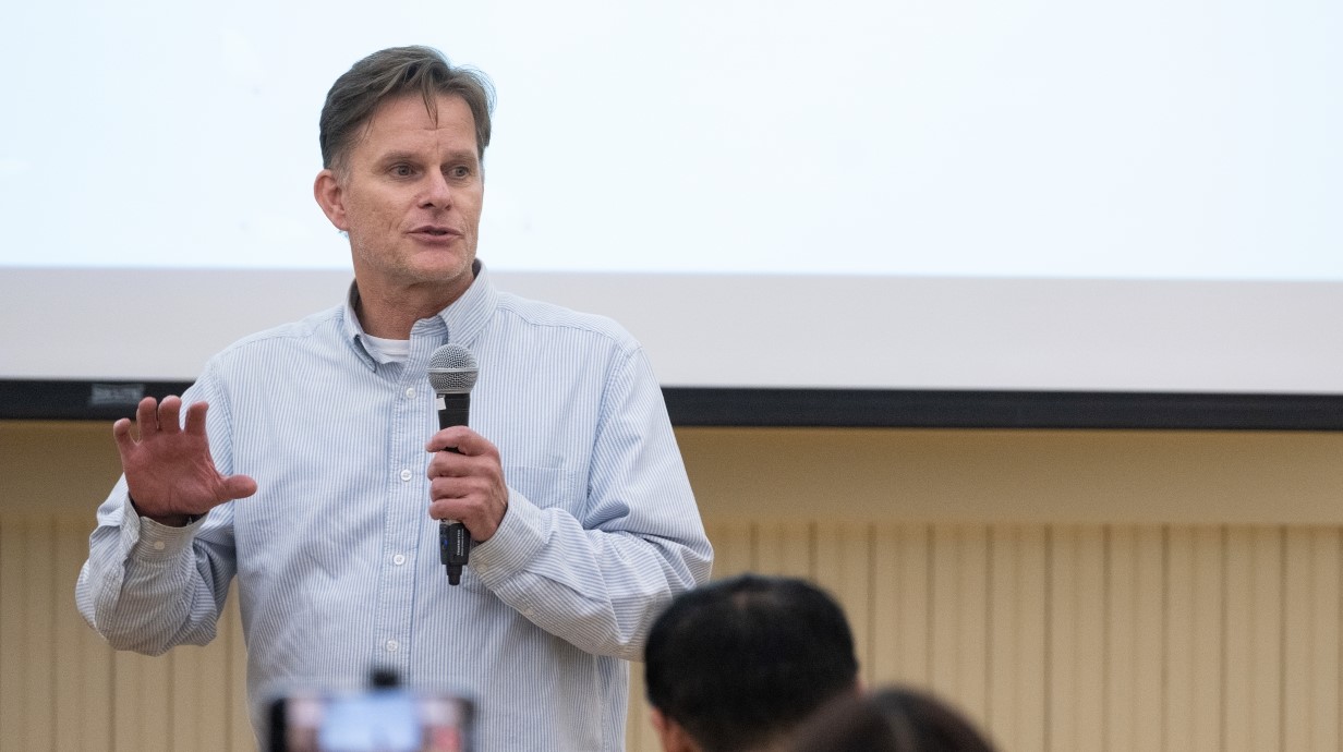 image of a professor standing in front of a classroom holding a microphone and speaking to a crowd