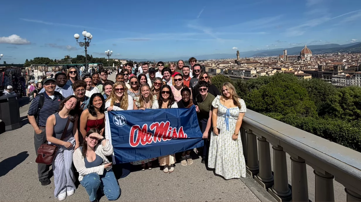 Concert Singers in Italy pose for a group photo holding an Ole Miss flag