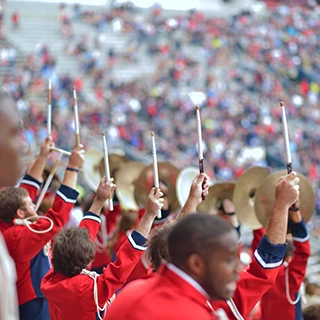Drumline holds up their drumsticks in the stands during a home game