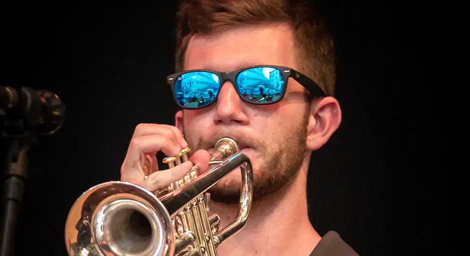 Close up of man playing trumpet with reflective blue sunglasses.