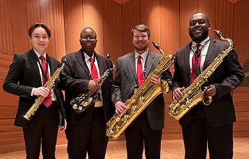 Saxophone quartet poses for a photo holding their instruments and smiling