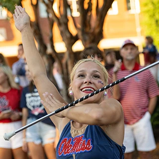 A feature twirler jumps with two flaming batons during a halftime performance at Vaught-Hemingway Stadium