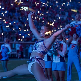 A feature twirler jumps with two flaming batons during a halftime performance at Vaught-Hemingway Stadium