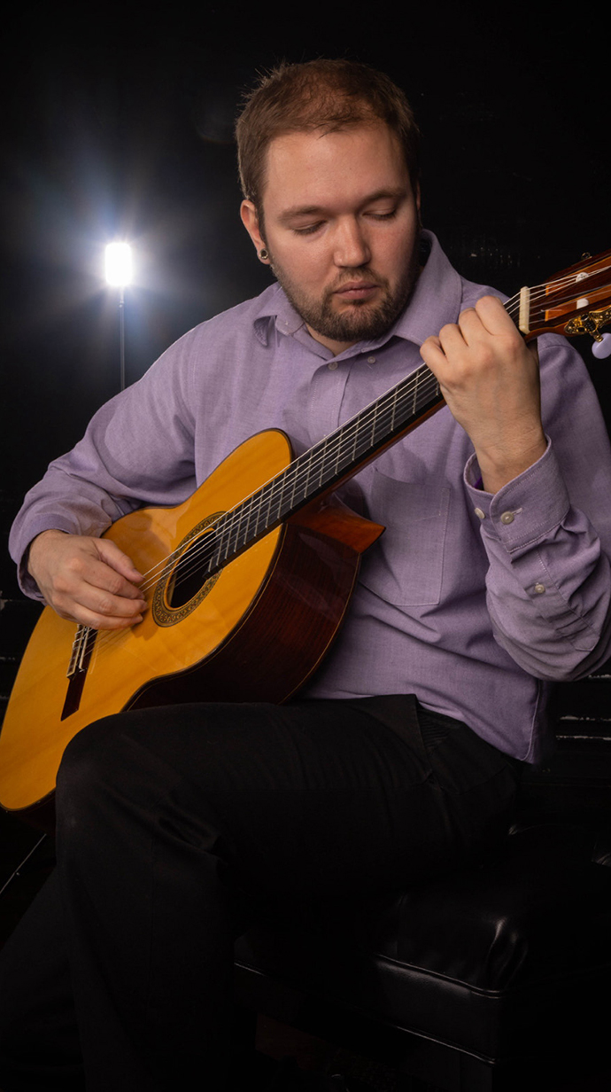 A young man plays guitar on a stage.