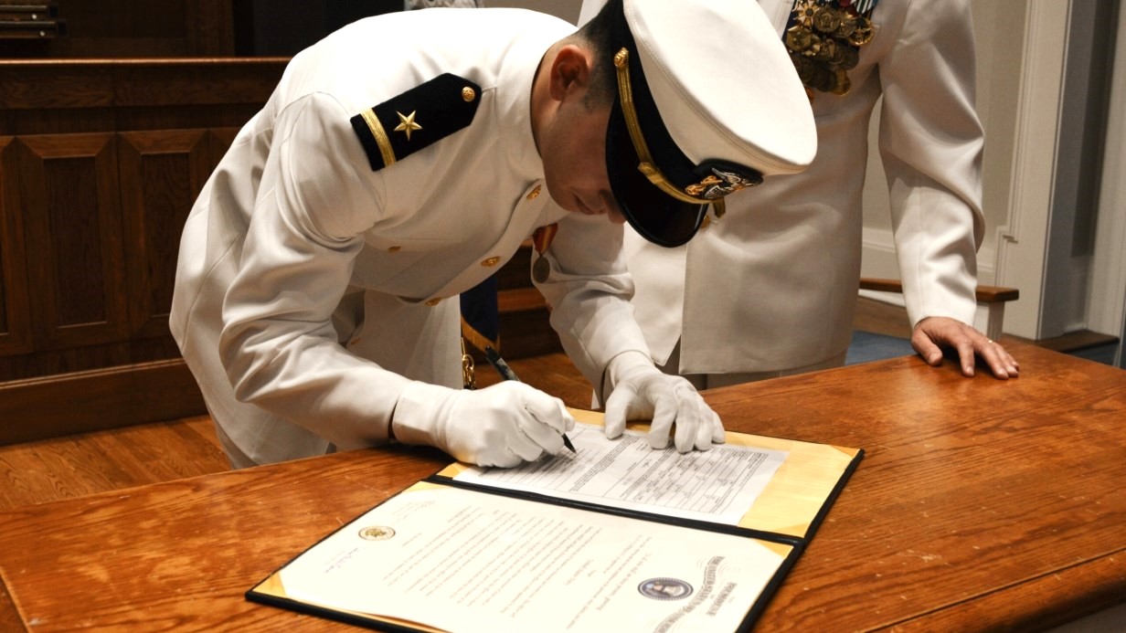 image of a commissioned officer signing the contract while in white dress uniform