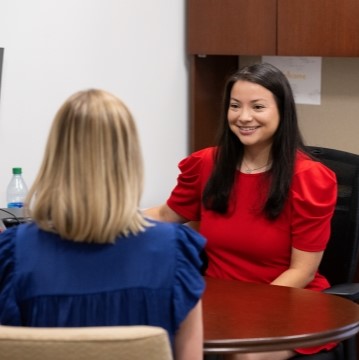 image of advisor seated at her desk and smiling at a student 