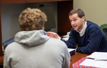 image of professor seated in his office talking with a student