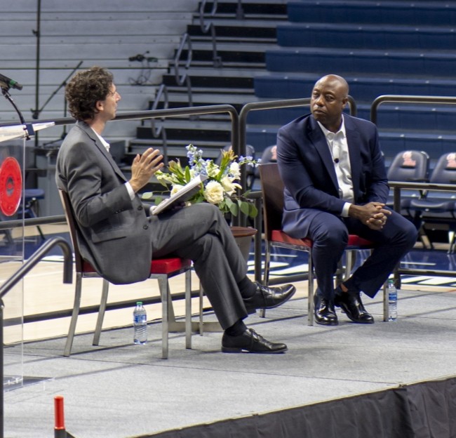 two men in suits talk on stage
