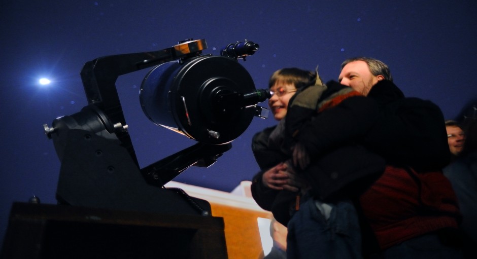 young boy is being held up so he can look through a telescope at night
