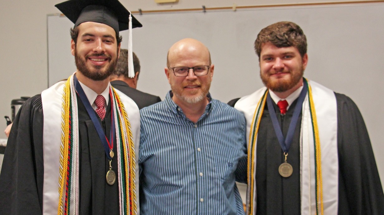 faculty member standing with two students in graduation robes