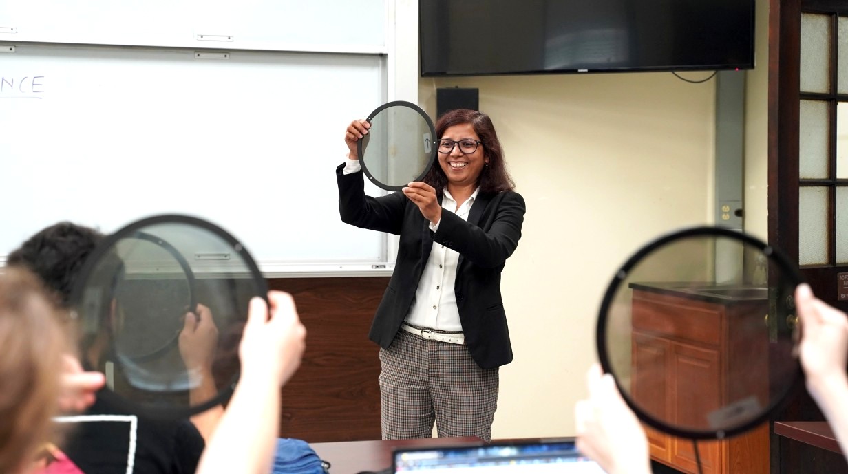 professor in front of class holding up large lens and students holding up their own lenses