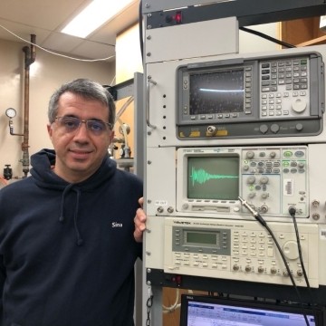 image of doctoral student standing next to rack of equipment in a lab