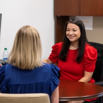 Two women talking to one another while seated at a desk