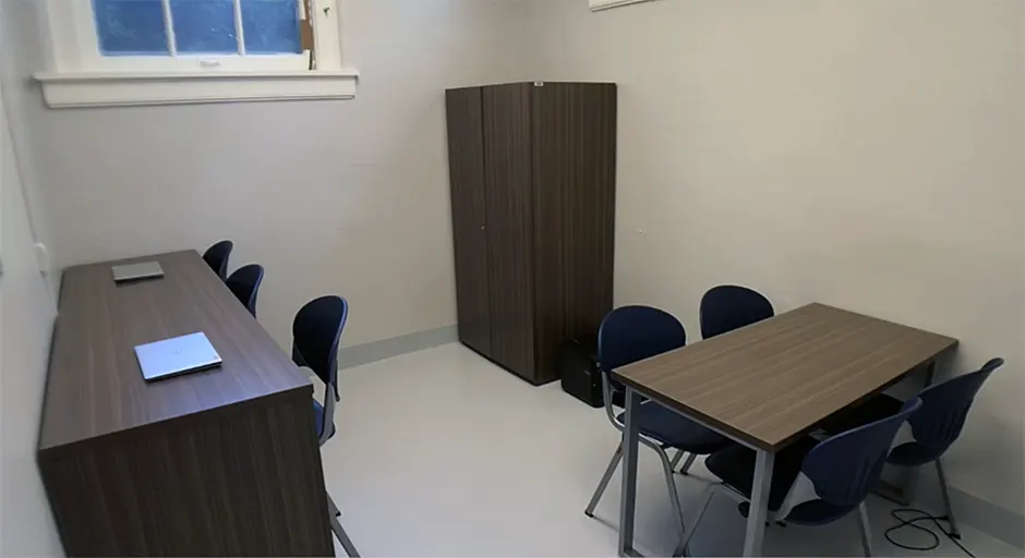 White room with table and chairs; laptop station with 2 chairs; and a wooden storage cabinet.