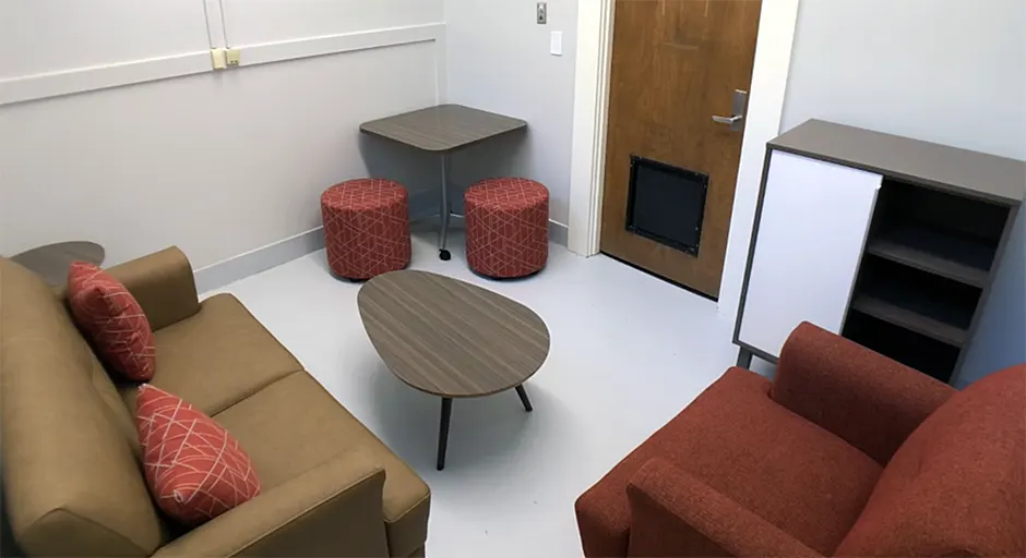 white room with small sofa and pillows; large chair; coffee table, and small table with two stools.