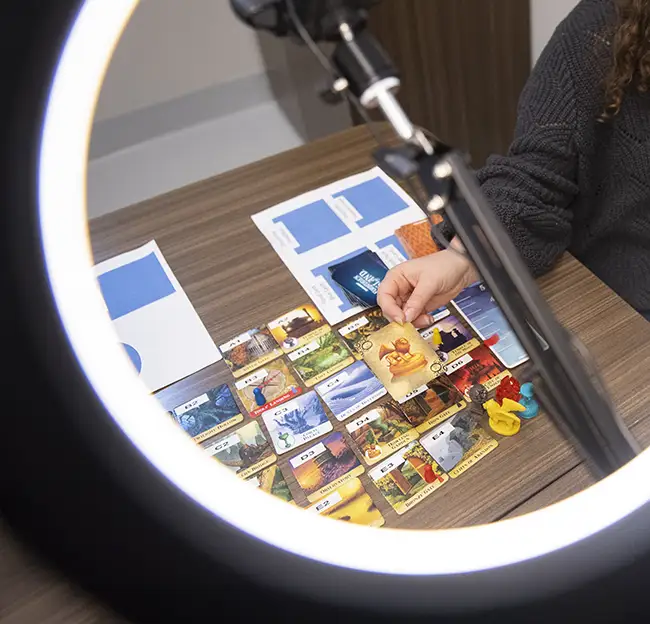 Experiment set up; magnifying light lighting up a hand and some cards on a desk. 