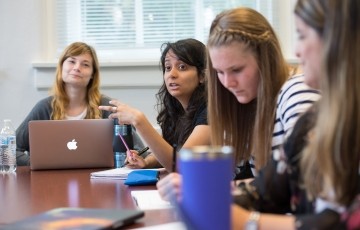 students seated around a table talking in a graduate class