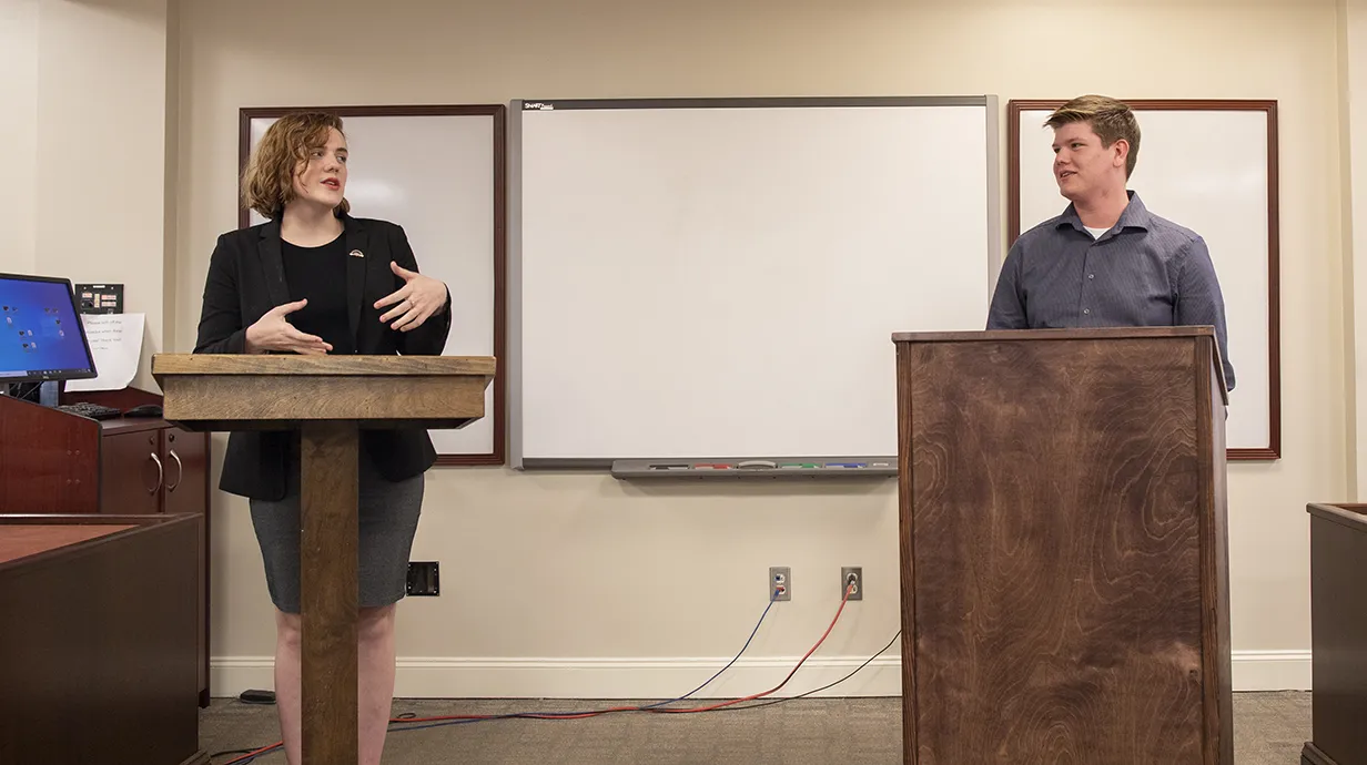 Two students behind podiums in classrooms having a conversation. 