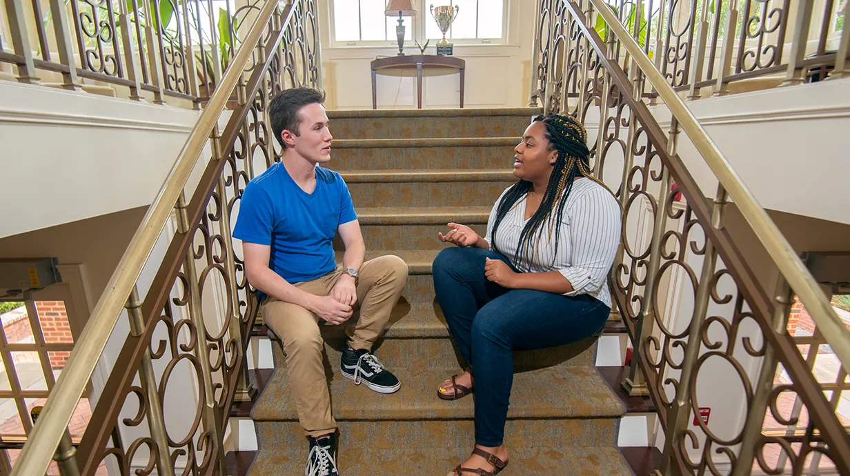 Two students sitting on stairs having a conversation.