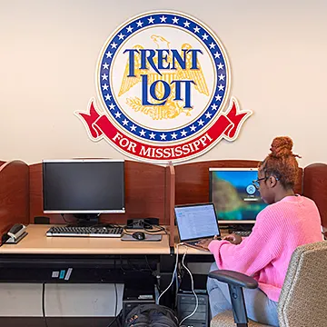 Student in computer lab seated with back turned to camera. Big round sign on the wall says "Trent Lott for Mississippi"