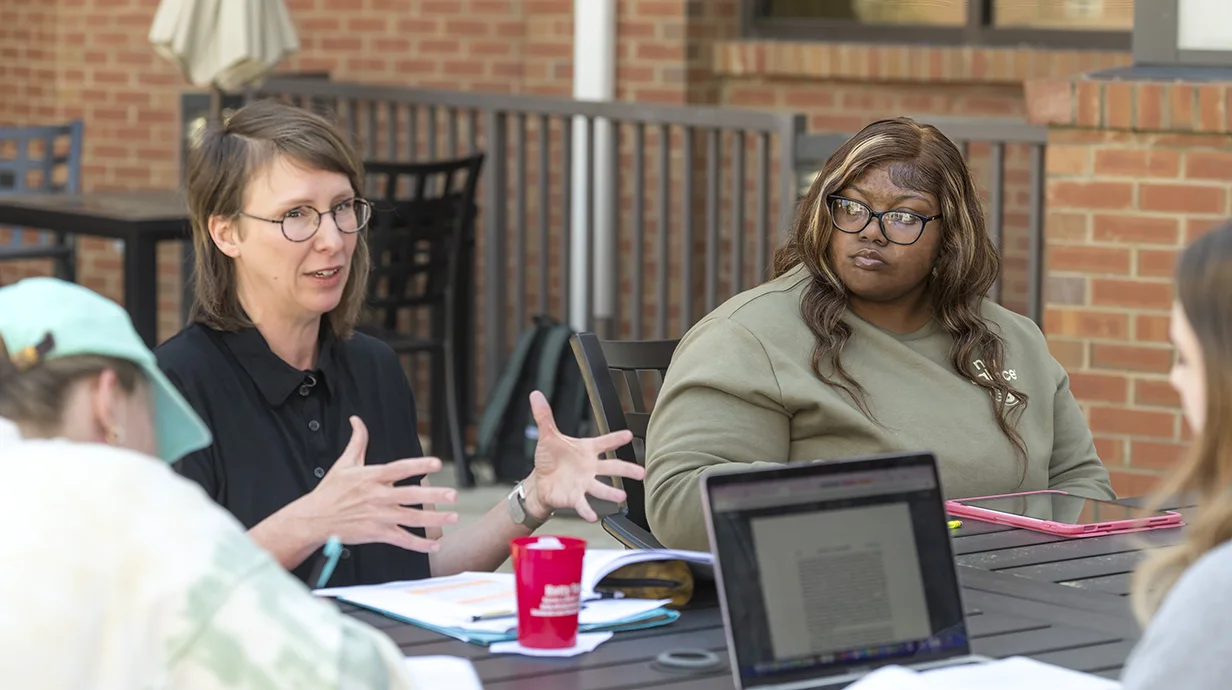 image of professor and a few students seated at an outdoor table having class