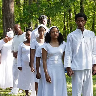 Group of people wearing white as part of a ritual walking outside.