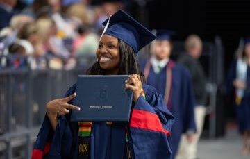 image of a student at graduation wearing cap and gown and holding diploma cover