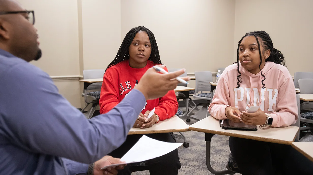 professor sitting with two students in a classroom