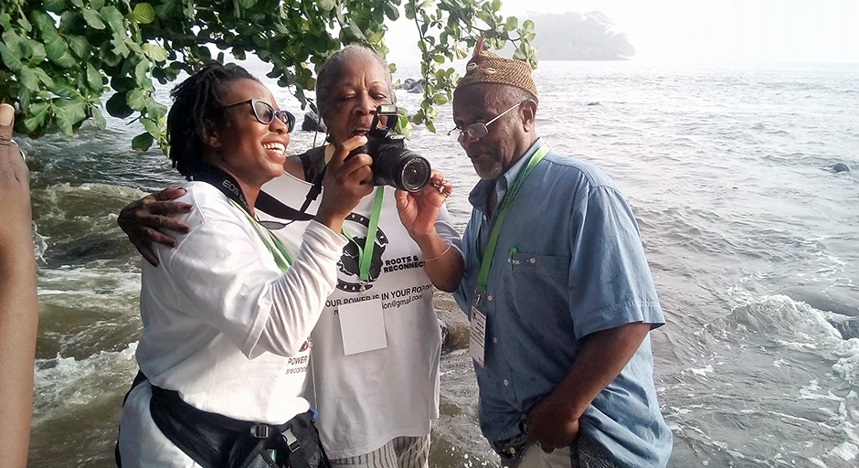 3 people stand at rushing water's edge looking at a camera