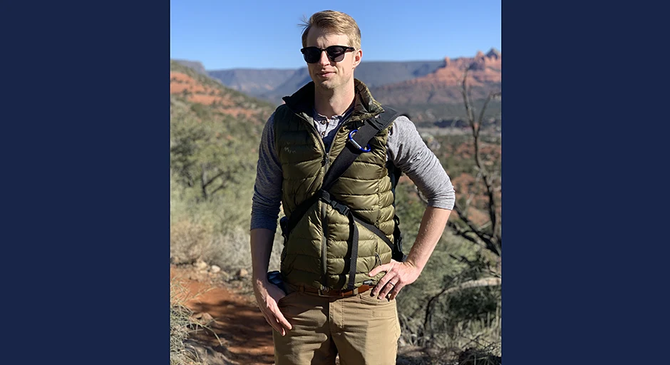 Person with sunglasses and vest standing with mesa-type mountains in background