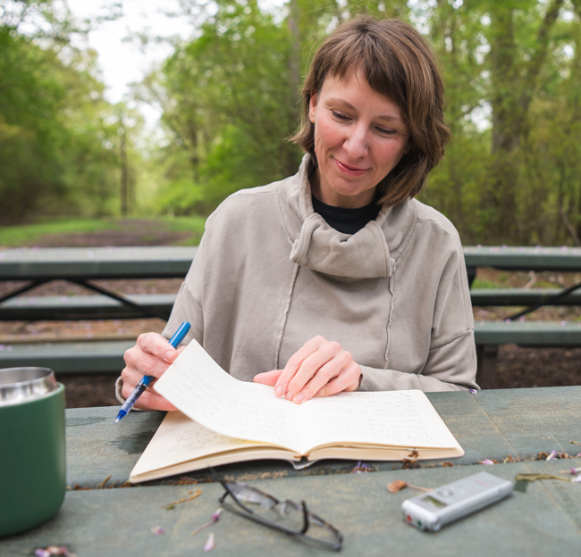 image of Amy McDowell writing in a notebook at a bench outside