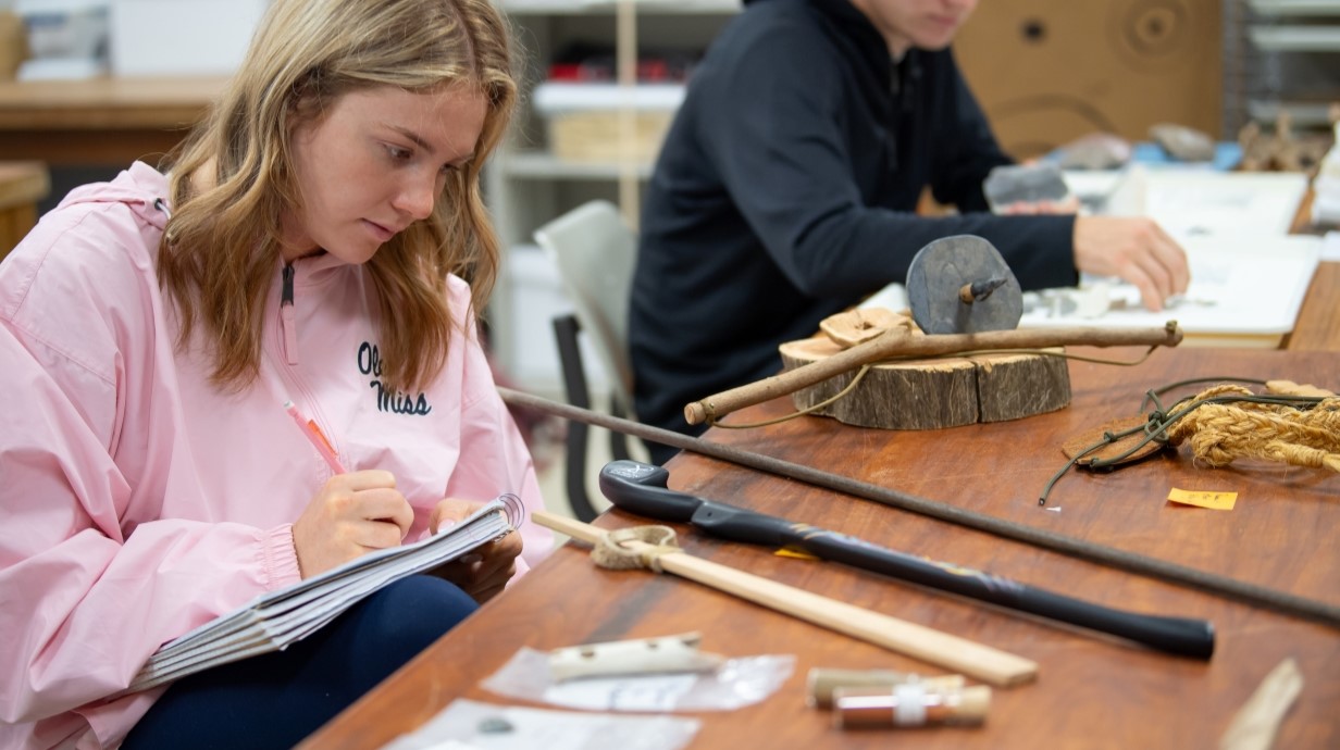 image of a student making notes with archaeological artifacts on the table
