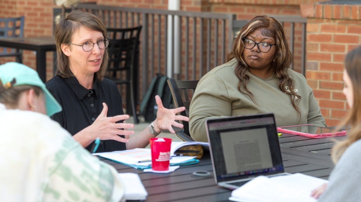 image of professor and a few students seated at an outdoor table having class