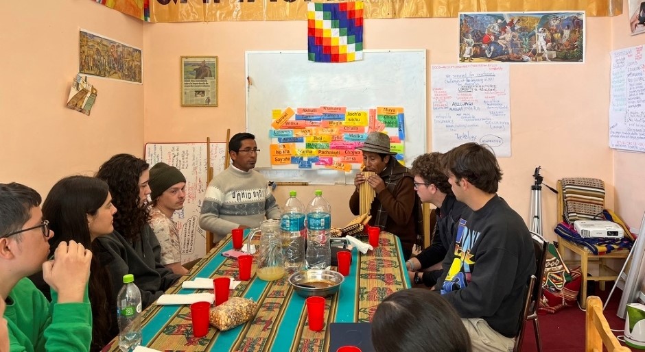 image of students sitting around a table with a man playing the pan flute