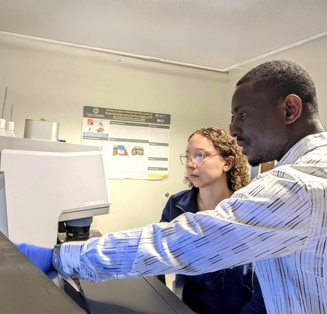 faculty and student standing in a lab working a machine