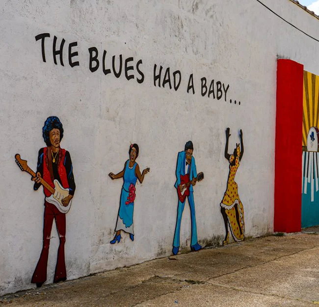 Mural of musicians and singers (4 figures) on side of a white building; text reads "The Blues Had a Baby..." 