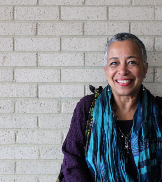 smiling portrait of Barbara Phillips standing against white brick wall