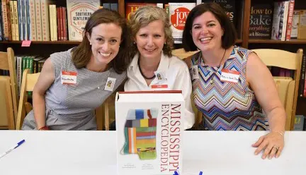 Three people at desk with "Mississippi Encyclopedia" book in foreground on table.