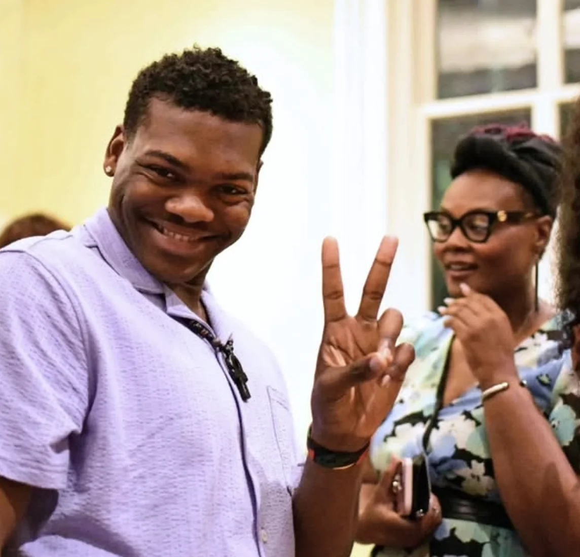 two people at reception; person in foreground smiling and showing "peace fingers"