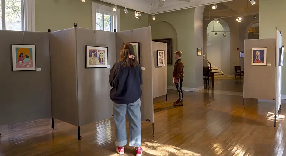 two people stand in gallery looking at art on partitioned walls