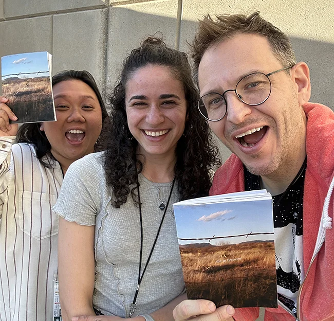 3 people looking at camera and smiling. Person on right holds a brochure